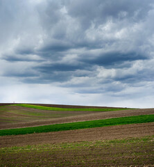 Wall Mural - Colored lines and hills of spring fields under a beautiful storm sky with contrasting clouds.