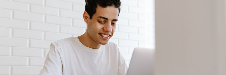 Sticker - Smiling young hispanic man working studying on laptop