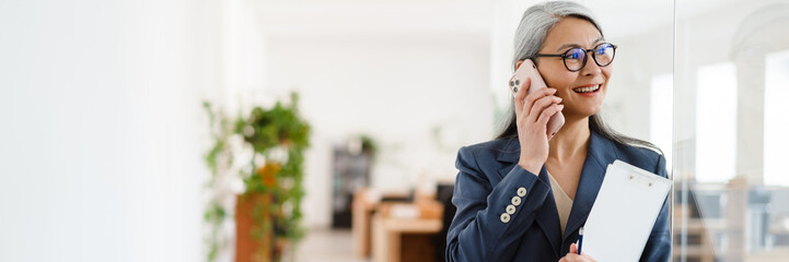 the happy asian woman talking on the phone while looking to the side in a light office