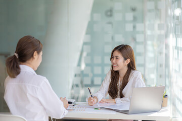 Two women sitting through white papers and talking, two business women discussing brainstorming and planning operations, form a partnership to form a startup company. Management of startup company.