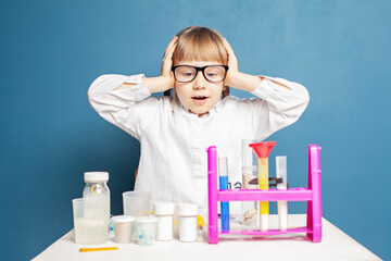 Wall Mural - Funny kid schoolgirl doing science experiments on blue background. Science and education concept