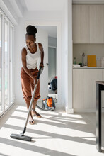 Black Woman Vacuuming Floor Near Kitchen Window
