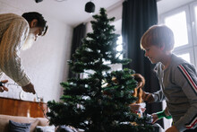 Boy Trying Helping To Grandpa Decorate Fir Tree 
