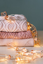 Stack Of Knitted Sweaters With Fairy Lights Garland.