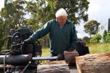 Logs Being Split By Senior On Rural Property