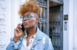 © Luis Velasco/Stocksy - Black Woman With Glasses On A Call On The Street.