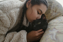 Sweet Girl With Braids Kissing Black Cat Lying On Couch