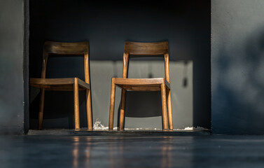 Two wooden chairs standing front of green cement wall at an empty room through which a ray of light passes. Space for text, Selective focus.