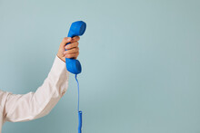 Human Hand Holding Retro Phone Receiver Against Copy Space Background. Cropped Shot Of Young Man Holding Blue Landline Telephone Receiver On Light Blue Copyspace Background. Customer Support Concept