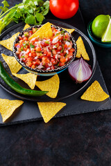 Wall Mural - Mexican Pico de Gallo salsa and ingredients. Bowl of tasty Pico de Gallo salsa and nachos on dark background. Top view. Copy space