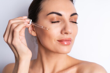 Close beauty portrait of topless woman with perfect skin and natural make-up, holds serum for youth and skin hydration, dropper with cosmetic oil.