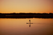 © Юля Бурмистрова - Silhouette of woman doing sup boarding alone on lake at sunset time holding oar in hands with charming yellow orange sky, water and trees in background. Active lifestyle.