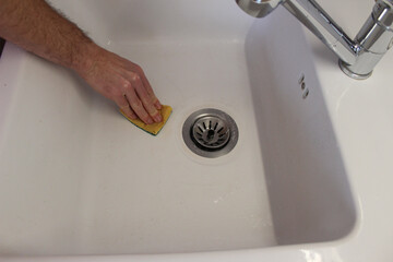 Poster - A closeup shot of a human hand washing a ceramic sink with a sponge