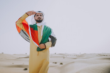 Wall Mural - Handsome man from the emirates making a safari in the Dubai desert. Young man wearing the traditional kandura dress walking on the dunes