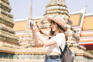 Wall Mural - Young adult asian woman traveller wear hat and backpack using camera for photo journey