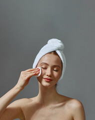 beautiful young girl with towel on head hold cotton pad cleansing face skin remove makeup, enjoy ski