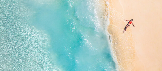 Wall Mural - Aerial view of a woman relaxing on tropical beach Maldives islands. Vacation adventure aerial beach landscape, turquoise water, soft sand. Amazing top view from drone beach shore azure lagoon seaside