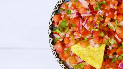 Wall Mural - Bowl with Pico de Gallo sauce rotates on white background. Tasty Pico de Gallo salsa and nachos chips. Mexican food concept. Vertical video