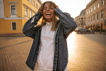 Wall Mural - Mad caucasian young girl ruffled her hair with hands while laughing in open area. Snow-white smile on face of tanned blonde. People sincere emotions lifestyle concept.