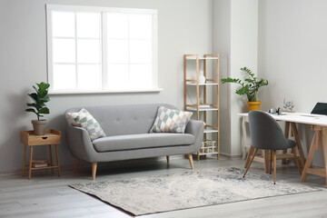 Interior of light living room with comfortable sofa and modern workplace