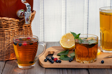 Wall Mural - Homemade mushroom kombucha drink in a jar with a tap and in glasses with mint, berries and lemon on a wooden table