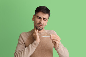 Canvas Print - Ill young man measuring temperature on green background