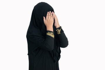 Wall Mural - Little Muslim girl wearing traditional black clothes Hijab or Nigab makes traditional prayer to God gesture over white background, with clipping path, 