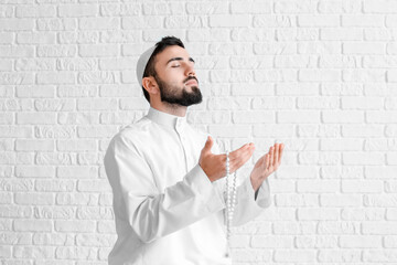 Wall Mural - Praying young Muslim man on white brick background