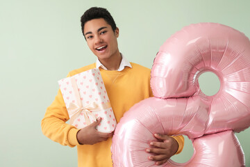 Canvas Print - African-American man with gift box and balloon in shape of figure 8 on light background. International Women's Day celebration