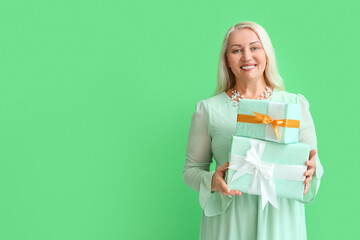 Poster - Fashionable mature woman holding stack of gift boxes on green background. International Women's Day celebration