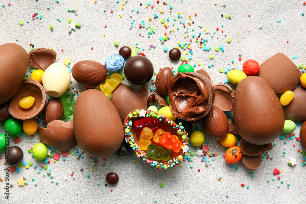 Composition with broken chocolate Easter eggs and different candies on light background