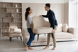 Happy married couple enjoying moving into new house. Excited homeowners, renters, man and woman carrying furniture, holding armchair, talking, joking, laughing, feeling joy. Relocation concept