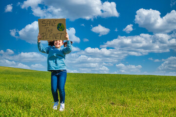 Beautiful Little girl In A Green Field With A Nice Blue Sky,  Holding A Cardboard Sign That Says SAVE THE PLANET. Image With Copy Space.