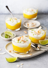 Sweet mango puree and cream cheese layered dessert decorated with roasted coconut chips and grated lime zest on glasses. Homemade healthy food concept.