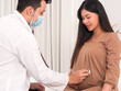 © Dollydoll - Asian doctor or gynecologist using stethoscope listening to baby's heart beat on mother's belly.
