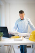 © epiximages - Architect with blue shirt is standing at height adjustable work table and is working