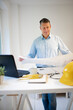 © epiximages - Architect with blue shirt is standing at height adjustable work table and is working