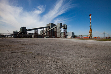 Metallurgy plant industrial building. Smelter and smoke stack. Gravel road on foreground. Blue sky with clouds background.