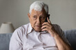 © fizkes - Serious concerned old grandpa talking on mobile phone, calling for emergency, ambulance. Senior 80s man speaking on cellphone, sitting on couch, at home, contact family on distance