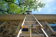 © Mary Salen - Low angle view of man on ladder cleaning  gutters of stone home