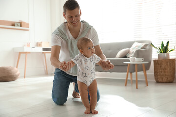 Wall Mural - Father supporting his baby daughter while she learning to walk at home