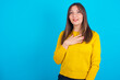 Joyful Young arab woman wearing knitted sweater over blue backgtound expresses positive emotions recalls something funny keeps hand on chest and giggles happily.