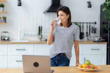 Portrait of Happy caucasian woman standing with glass of clean water at home kitchen. Healthy lifestyle, eating. looking away. friendly