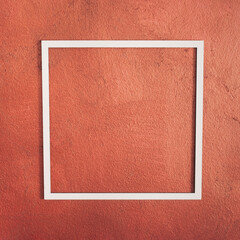 Square white frame on red bronze wall background. Side view. Creative concept, copy space.