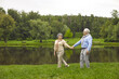 © Studio Romantic - Senior man and woman holding hands in the park, walking outdoors, happy elderly family. Elderly people walk near the river. Green grass, summer.