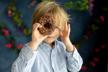 Cute little blond child, preschool boy, eating pink donut in the shape of heart, made for Valentine