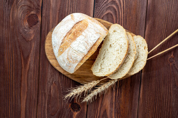 Close-up of fresh crispy wheat bread sliced lies on a wooden board. Wooden brown background. several ears of wheat are lying next to the bread. Top view, flat lay