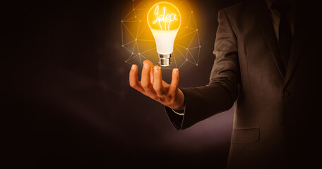 Poster - Idea Glowing Bulb In Business Man Hand with Dark Abstract Background. Futuristic and business concept backdrop