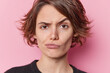 Headshot of serious beautiful young woman looks skeptical raises eyebrows purses lips considers something tries to make decision isolated over pink background. Human face expressions concept