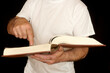 A man is standing, holding a book and poking at the page with his index finger.